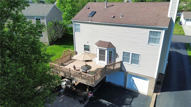 rear view of house with a deck, a garage, a shingled roof, asphalt driveway, and a chimney