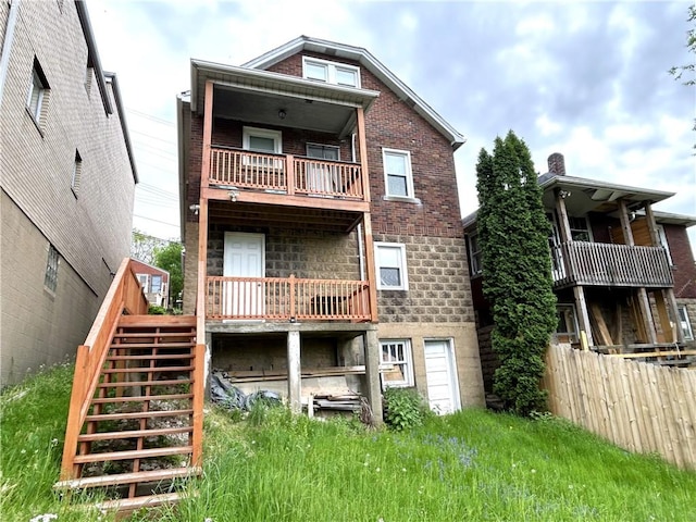 back of house featuring a balcony, stairs, fence, and brick siding