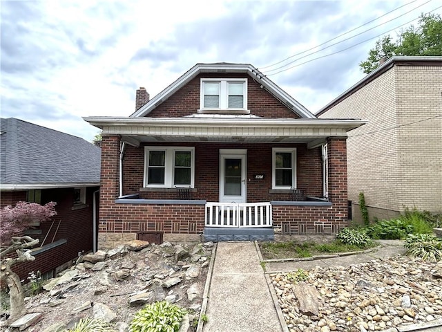 view of front of home with covered porch, a chimney, and brick siding