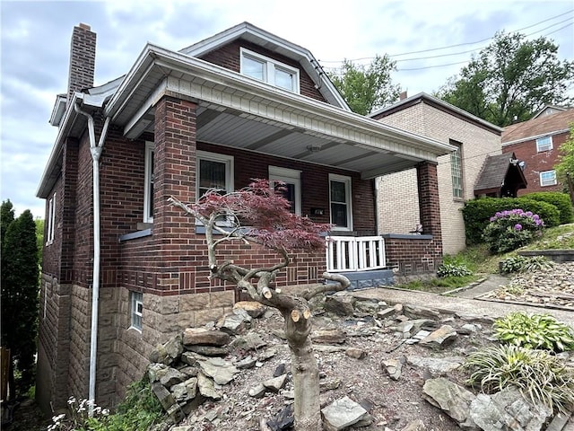 bungalow-style house featuring covered porch, a chimney, and brick siding