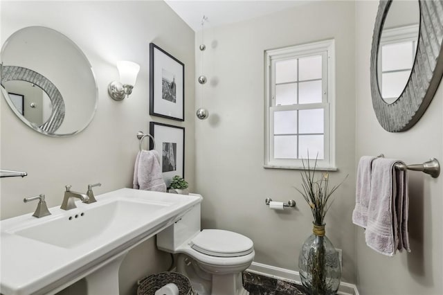 half bathroom with toilet, a sink, and baseboards