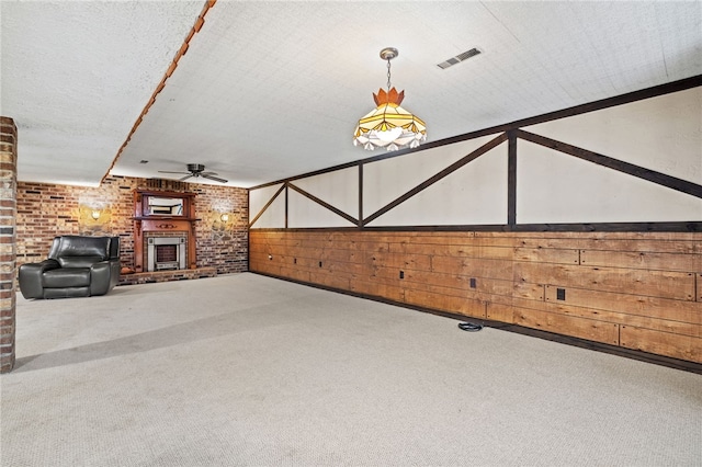 unfurnished living room with carpet, ceiling fan, a brick fireplace, and wood walls