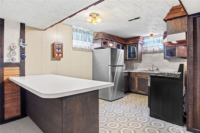 kitchen with freestanding refrigerator, black gas stove, a sink, under cabinet range hood, and a peninsula