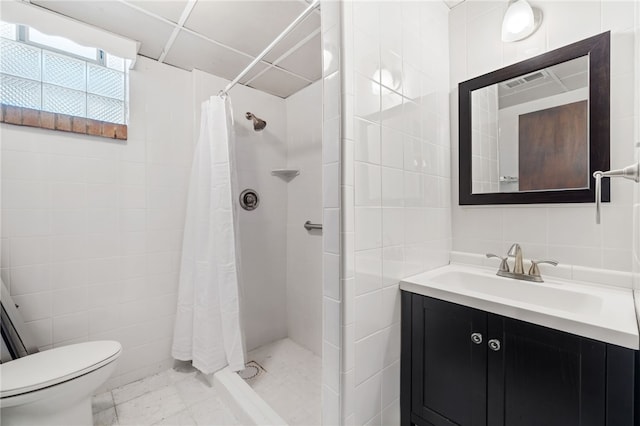 bathroom featuring tile walls, toilet, tiled shower, vanity, and marble finish flooring