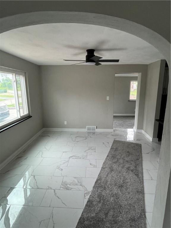 unfurnished room with arched walkways, light marble finish floors, a ceiling fan, and baseboards
