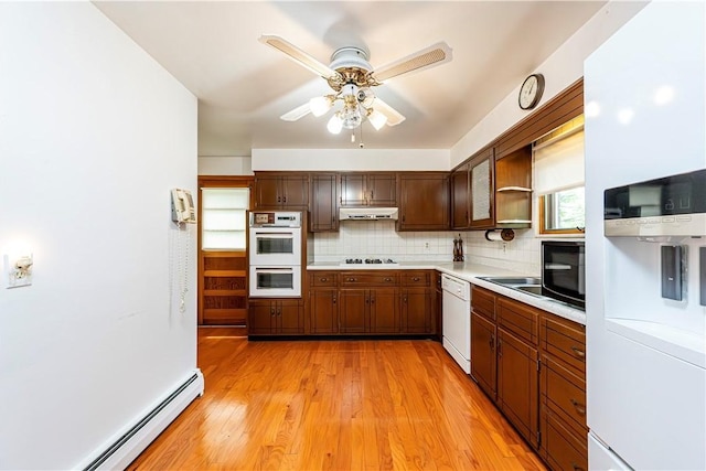 kitchen with white appliances, under cabinet range hood, a baseboard radiator, light countertops, and backsplash