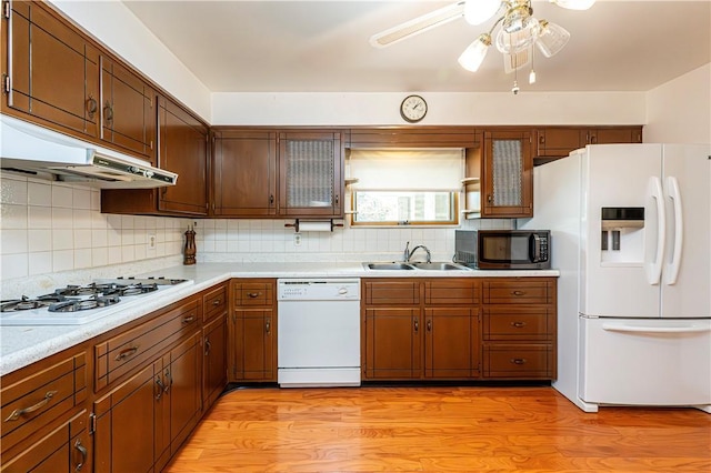 kitchen featuring white appliances, a sink, under cabinet range hood, and tasteful backsplash