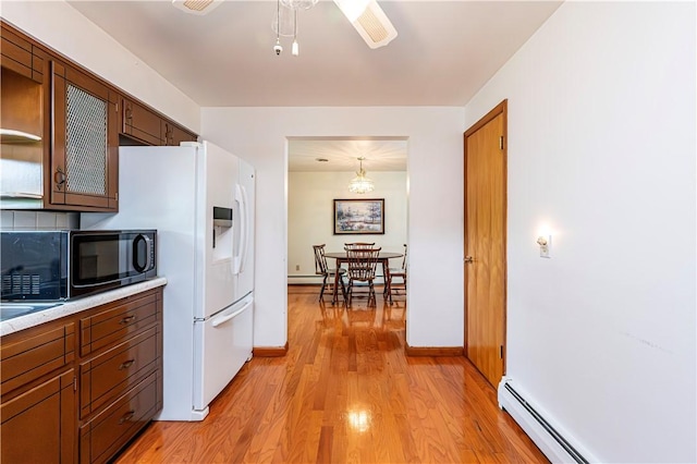 kitchen featuring black microwave, a baseboard heating unit, light wood-type flooring, light countertops, and white fridge with ice dispenser