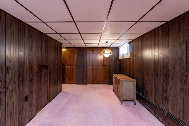 basement with wood walls, light carpet, and a paneled ceiling