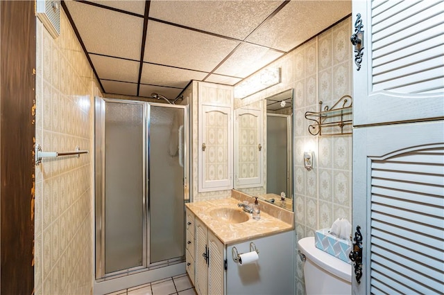 full bathroom with a stall shower, vanity, tile patterned flooring, toilet, and tile walls
