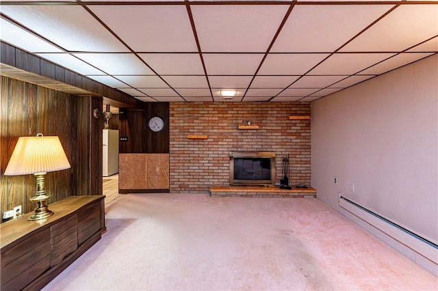 unfurnished living room with baseboard heating, a brick fireplace, wood walls, light carpet, and a paneled ceiling