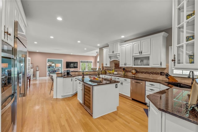 kitchen featuring a sink, dishwasher, light wood-style flooring, a peninsula, and white cabinets