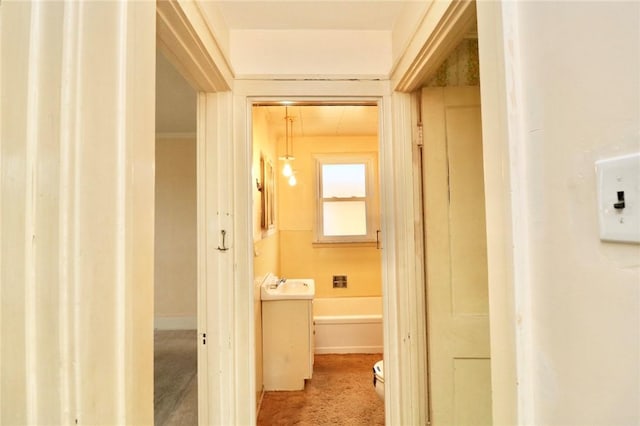 hall featuring baseboards, carpet flooring, and a sink
