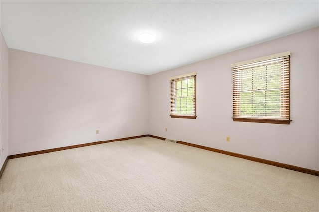spare room with baseboards and light colored carpet