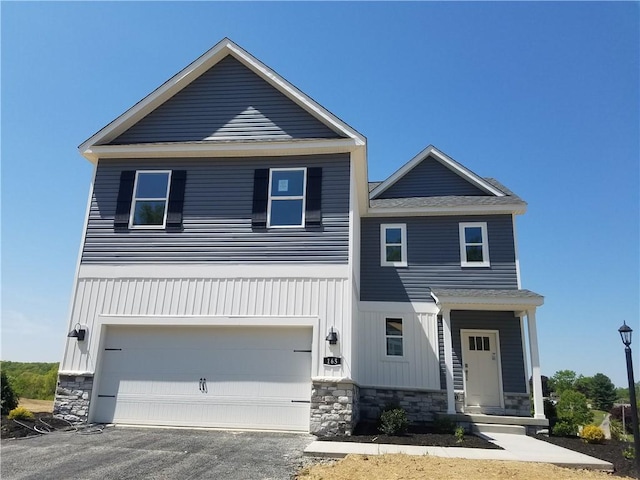 view of front of home with stone siding, an attached garage, board and batten siding, and driveway