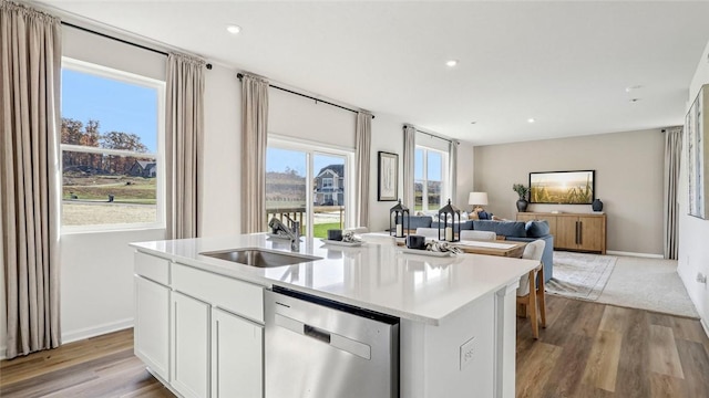 kitchen with dishwasher, a sink, a kitchen island with sink, wood finished floors, and light countertops