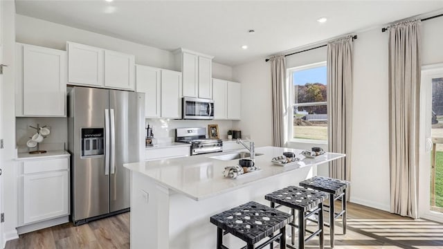 kitchen featuring stainless steel appliances, a sink, light wood-style floors, a kitchen bar, and a kitchen island with sink