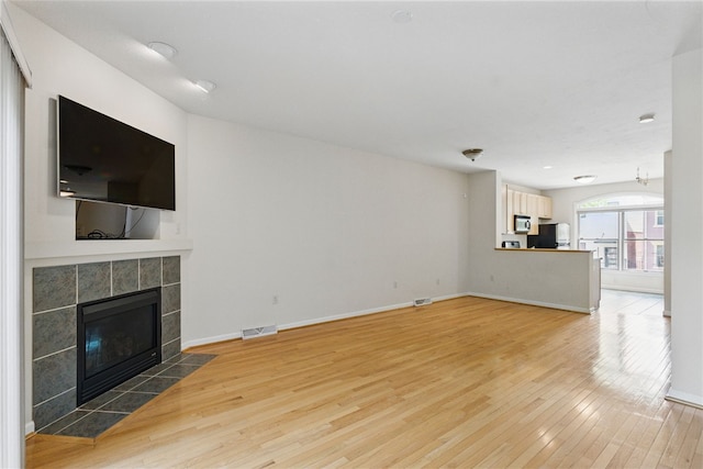 unfurnished living room featuring light wood-style floors, a tiled fireplace, and baseboards