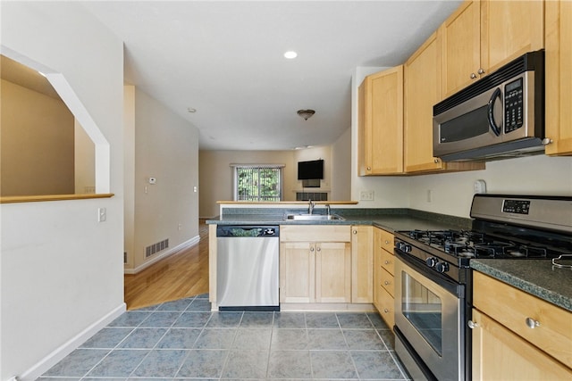 kitchen with appliances with stainless steel finishes, light brown cabinets, dark countertops, and recessed lighting
