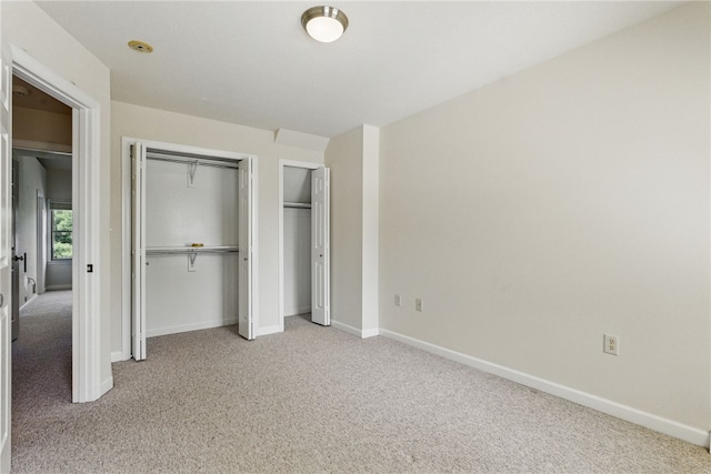 unfurnished bedroom with light colored carpet, baseboards, and two closets