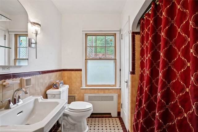 bathroom featuring radiator heating unit, a sink, tile walls, toilet, and wainscoting