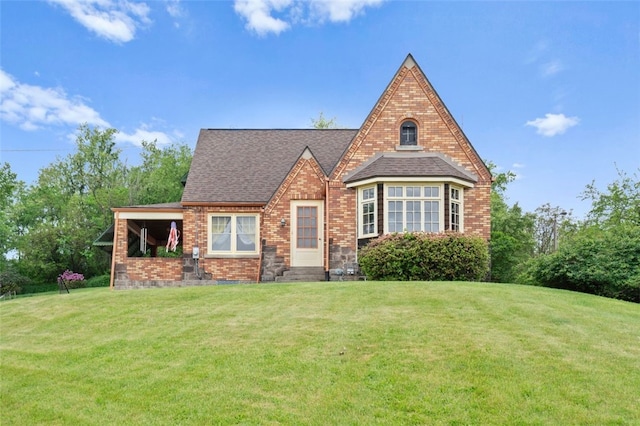 tudor house featuring a front yard, brick siding, and roof with shingles