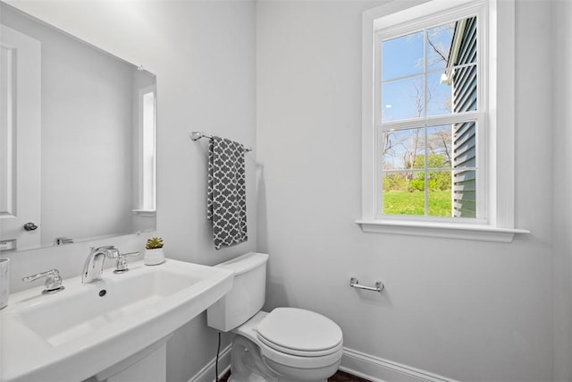 half bathroom with plenty of natural light, toilet, baseboards, and a sink