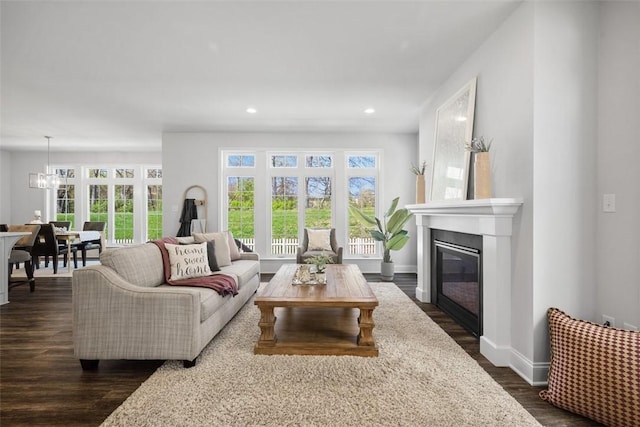 living room with recessed lighting, healthy amount of natural light, dark wood-type flooring, a glass covered fireplace, and baseboards