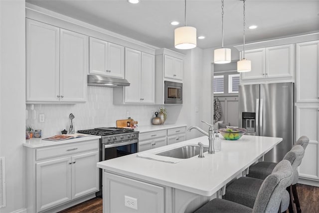 kitchen with under cabinet range hood, appliances with stainless steel finishes, a sink, a kitchen breakfast bar, and white cabinets