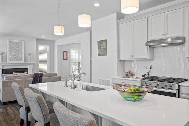 kitchen with under cabinet range hood, stainless steel range with gas cooktop, a sink, light countertops, and open floor plan