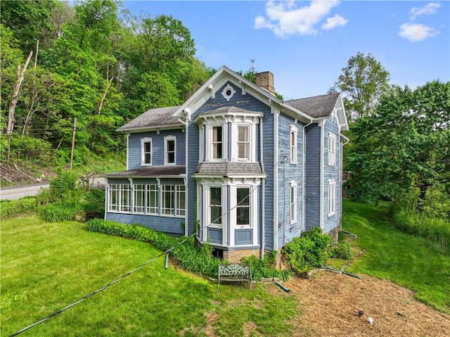 back of property featuring a chimney, a lawn, a sunroom, and roof with shingles