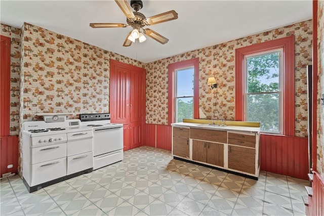 kitchen with electric stove, wallpapered walls, healthy amount of natural light, a ceiling fan, and a wainscoted wall