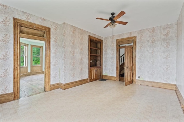 empty room with a ceiling fan, wallpapered walls, tile patterned floors, and baseboards