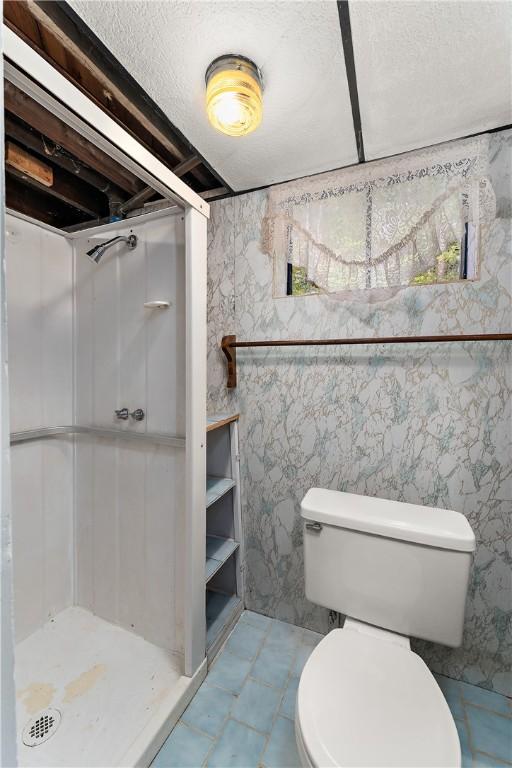 bathroom featuring toilet, a stall shower, and a textured ceiling