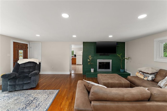 living room featuring baseboards, recessed lighting, wood finished floors, and a brick fireplace