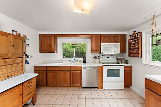 kitchen featuring white appliances, a sink, light countertops, light tile patterned floors, and healthy amount of natural light