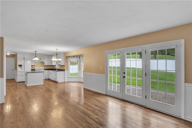 unfurnished living room with a chandelier, light wood-style floors, a wainscoted wall, french doors, and a sink