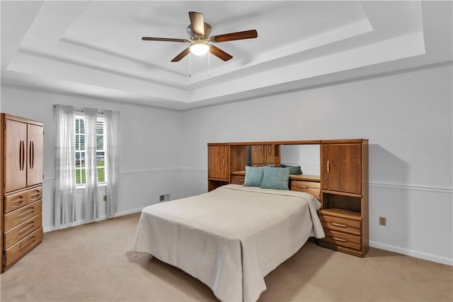 bedroom featuring a raised ceiling, light colored carpet, baseboards, and a ceiling fan