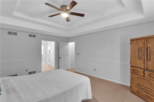 bedroom featuring a raised ceiling, light colored carpet, baseboards, and a ceiling fan