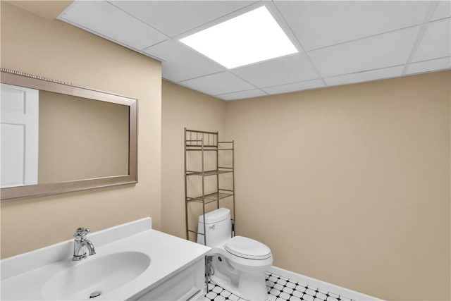 half bathroom with toilet, a drop ceiling, vanity, and baseboards