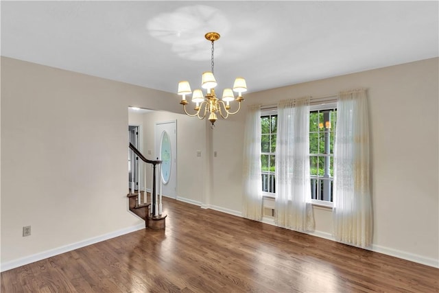 spare room featuring a chandelier, wood finished floors, baseboards, and stairway