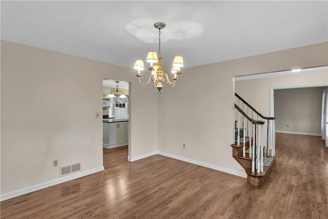 empty room with a chandelier, wood finished floors, baseboards, and stairs