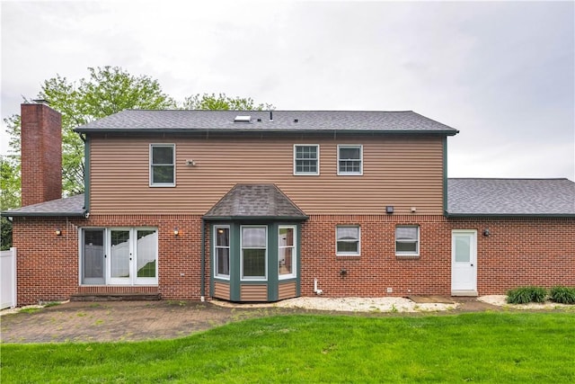 rear view of property featuring brick siding, a lawn, a chimney, a patio, and a shingled roof