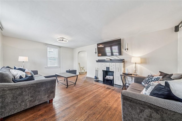 living area with arched walkways, wood finished floors, a brick fireplace, and baseboards