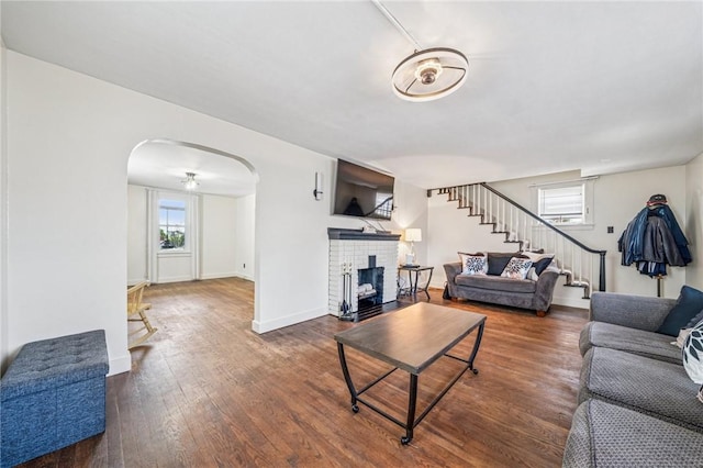 living area with stairway, wood finished floors, arched walkways, baseboards, and a brick fireplace