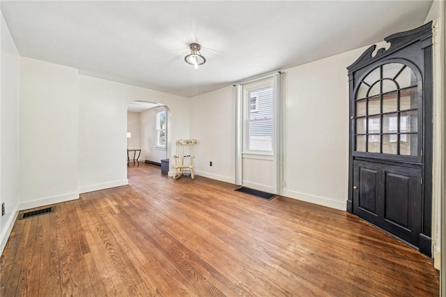 entrance foyer with arched walkways, wood finished floors, and baseboards