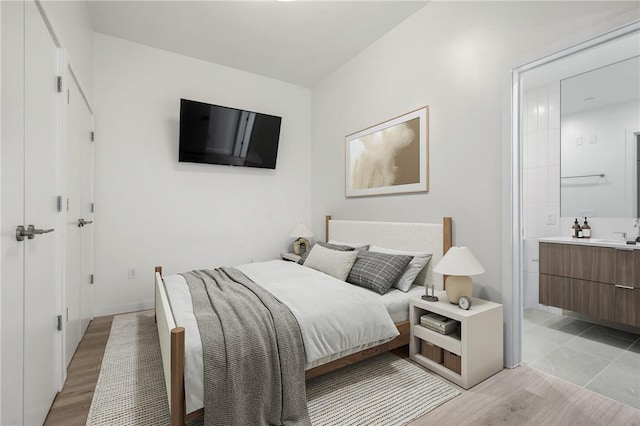 bedroom with connected bathroom, light wood-style floors, and a sink