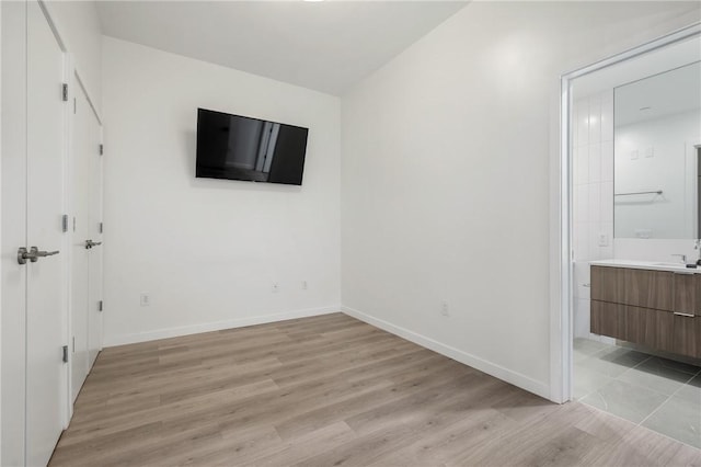 unfurnished bedroom featuring light wood finished floors, ensuite bath, baseboards, and a sink