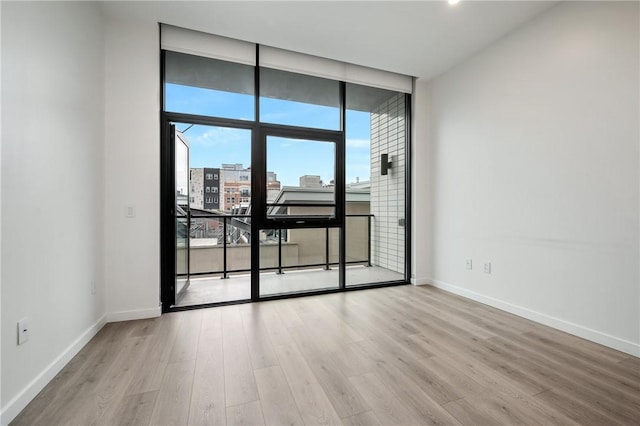 empty room featuring expansive windows, wood finished floors, baseboards, and a city view