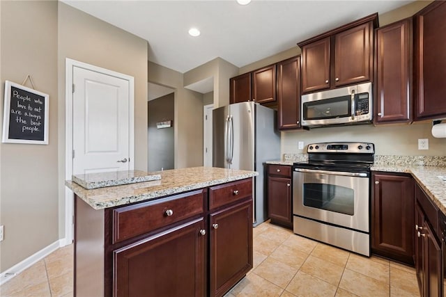 kitchen featuring appliances with stainless steel finishes, light tile patterned floors, light stone counters, a kitchen island, and dark brown cabinets